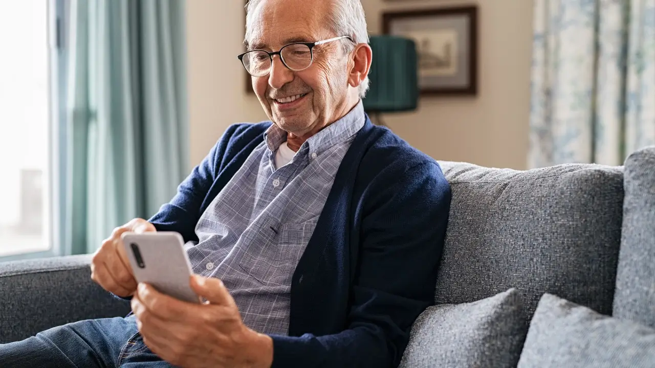 Idoso sorrindo enquanto usa um smartphone para idosos, navegando em apps de 2025.