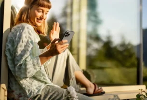 Mulher sorrindo enquanto usa o celular em um ambiente tranquilo, simbolizando o bem-estar diário com o celular.
