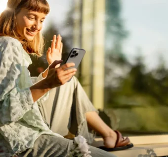 Mulher sorrindo enquanto usa o celular em um ambiente tranquilo, simbolizando o bem-estar diário com o celular.