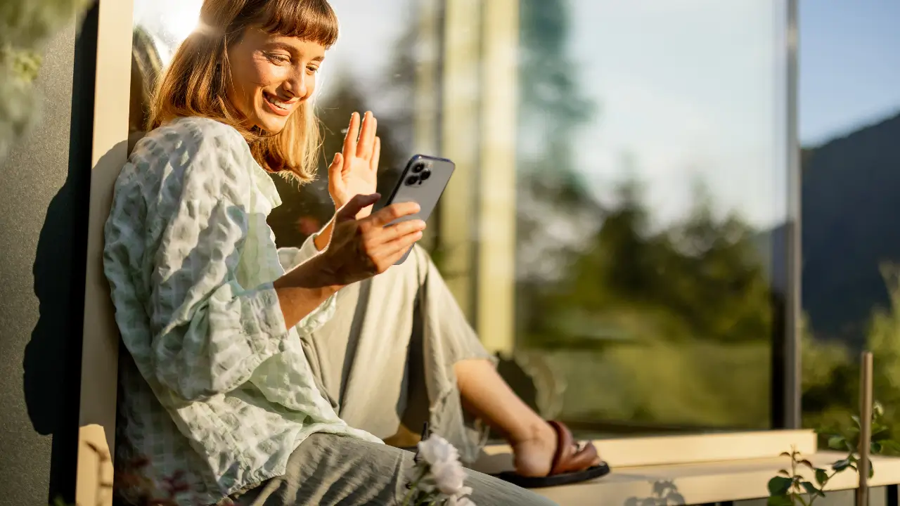Mulher sorrindo enquanto usa o celular em um ambiente tranquilo, simbolizando o bem-estar diário com o celular.