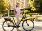 Uma pessoa sorridente numa bicicleta elétrica, numa cidade sustentável ao fundo.