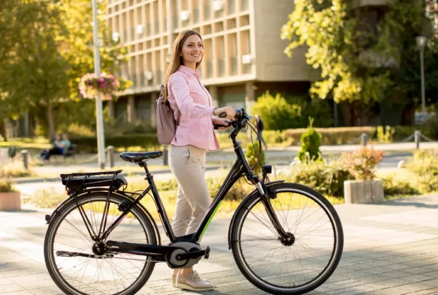 Uma pessoa sorridente numa bicicleta elétrica, numa cidade sustentável ao fundo.